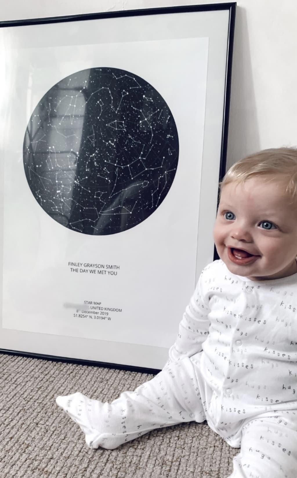 A baby sitting next to a framed star map